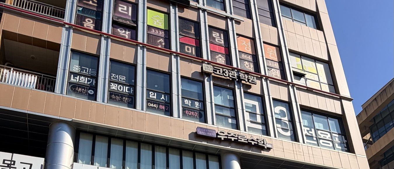 다정프라자 건물 바깥. 4층 창에 「중고등 전문 너희가 꽃이다 입시 학원」과 「고3관 학원」 간판이 붙어 있습니다