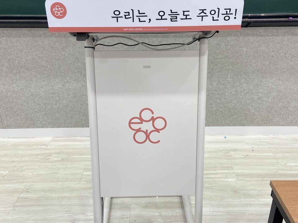 강의실 단상. 너희가 꽃이다 꽃 로고와 「우리는, 오늘도 주인공!」 문구가 붙어 있습니다